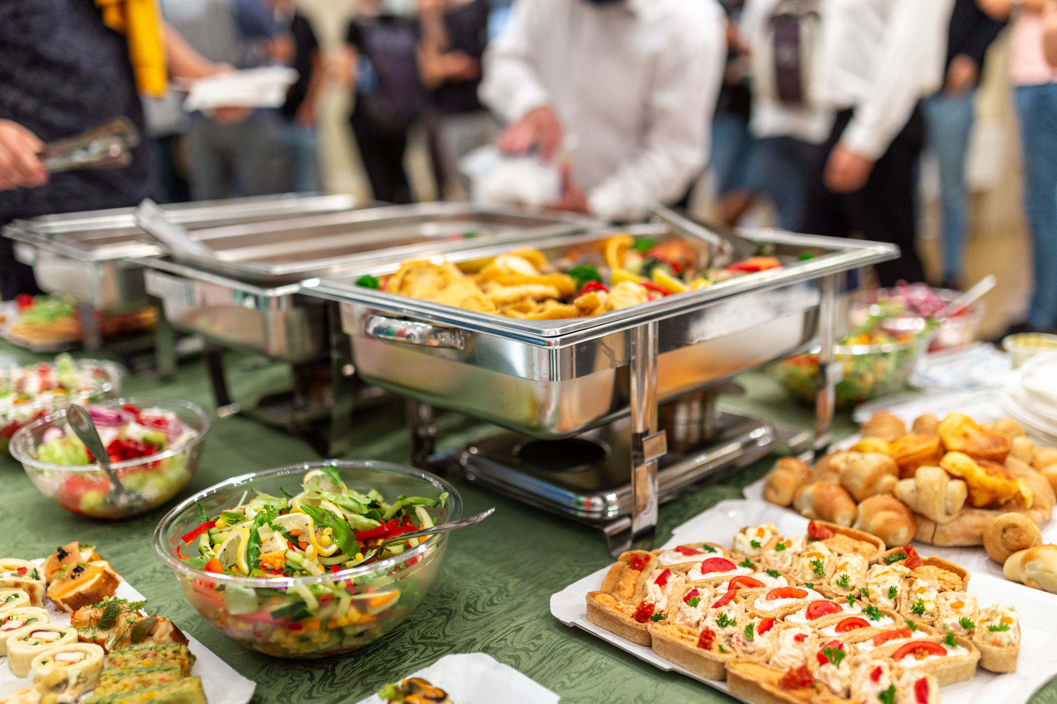 Warming tray with food and people in the background. Party lunch or dinner concept.